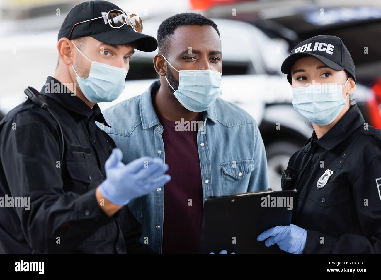 African american victim in medical mask standing near police officers with clipboard on urban street Stock Photo