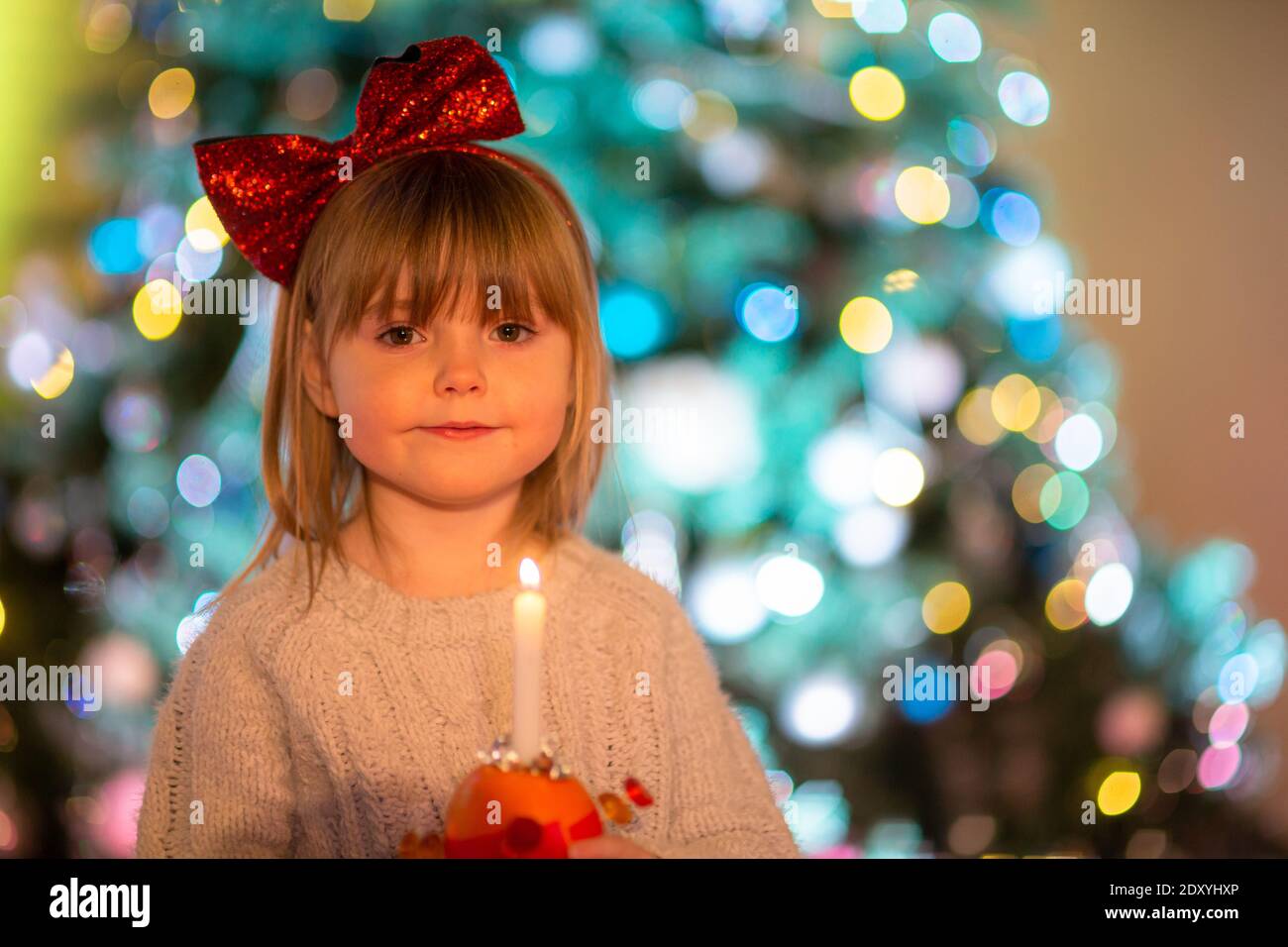 Cradley Heath, West Midlands, UK. 24th Dec, 2020. Four-year-old Hermione Hadlington stands proudly with her Christingle orange during the Christmas Eve service for children at Holy Trinity church, Cradley Heath, West Midlands. In the Christingle service the orange represents the world, the red ribbon symbolises the love and blood of Christ, the sweets represent all of God's creations, and the lit candle represents Jesus's light in the world, bringing hope to people living in darkness. Credit: Peter Lopeman/Alamy Live News Stock Photo