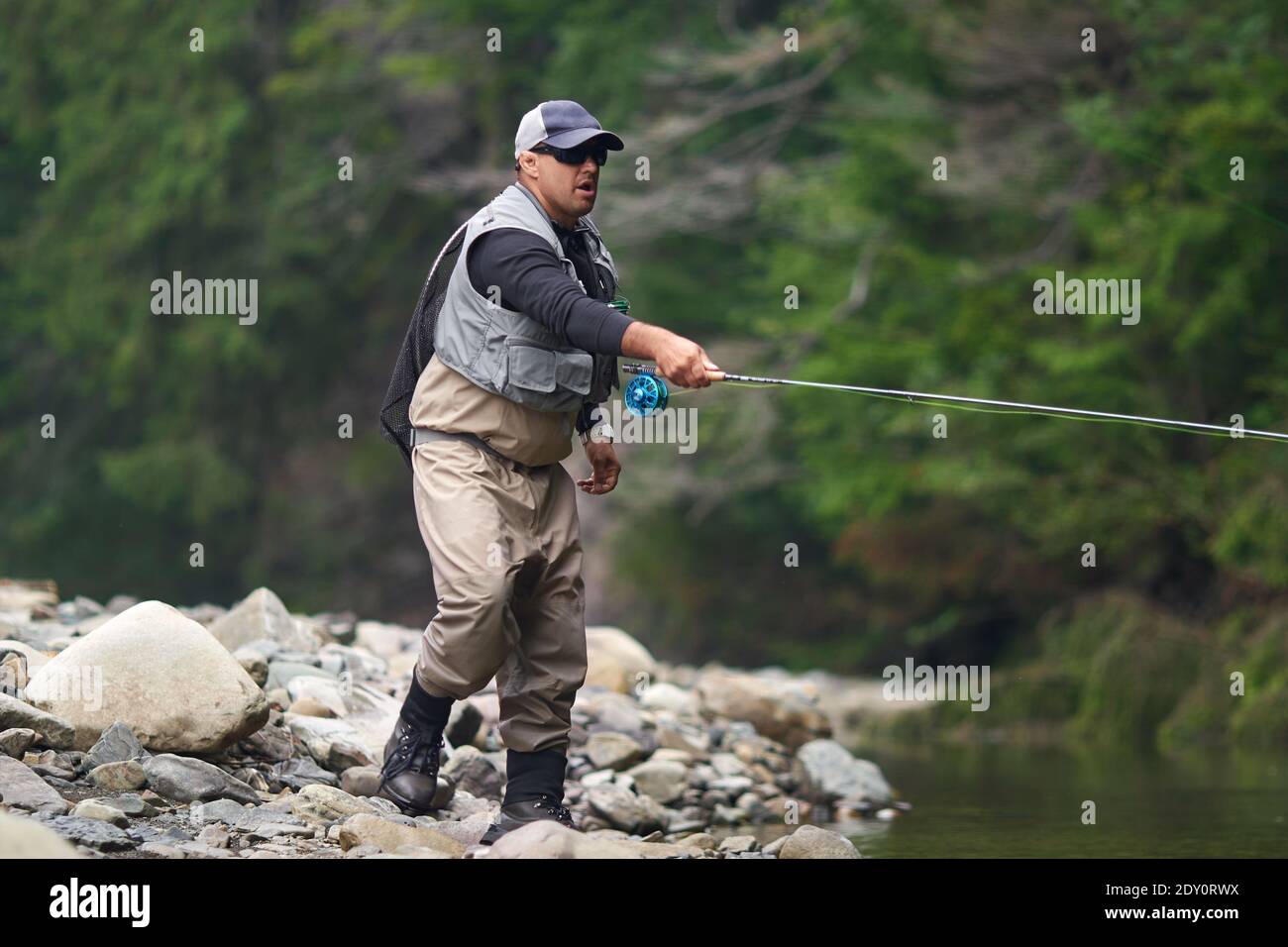 https://c8.alamy.com/comp/2DY0RWX/competent-fishermen-in-cap-glasses-and-waterproof-outfit-fishing-with-rod-among-mountains-man-standing-in-river-and-catching-fish-on-hook-2DY0RWX.jpg