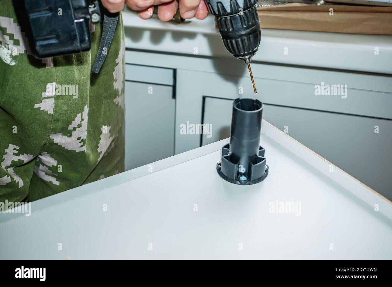 assembling furniture, a person fixes a table leg. Men's hands fasten a plastic furniture leg with a screwdriver. Selective focus. Stock Photo