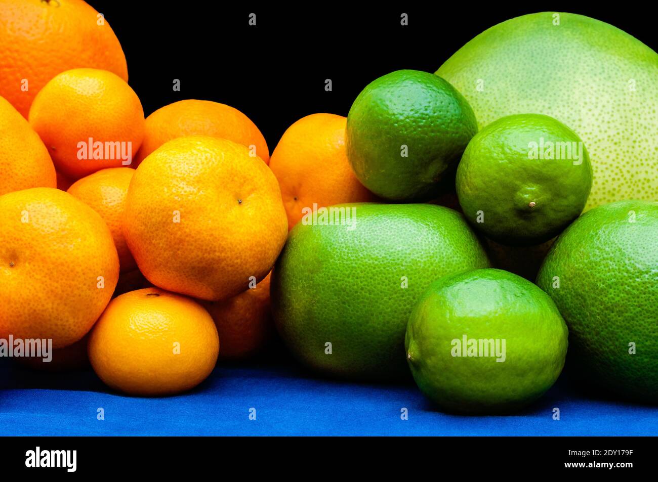 Isolated orange and green color groups citruses fruits on black background. Oranges, tangerines, limes, pomelo, grapefruits on blue tablecloth Stock Photo