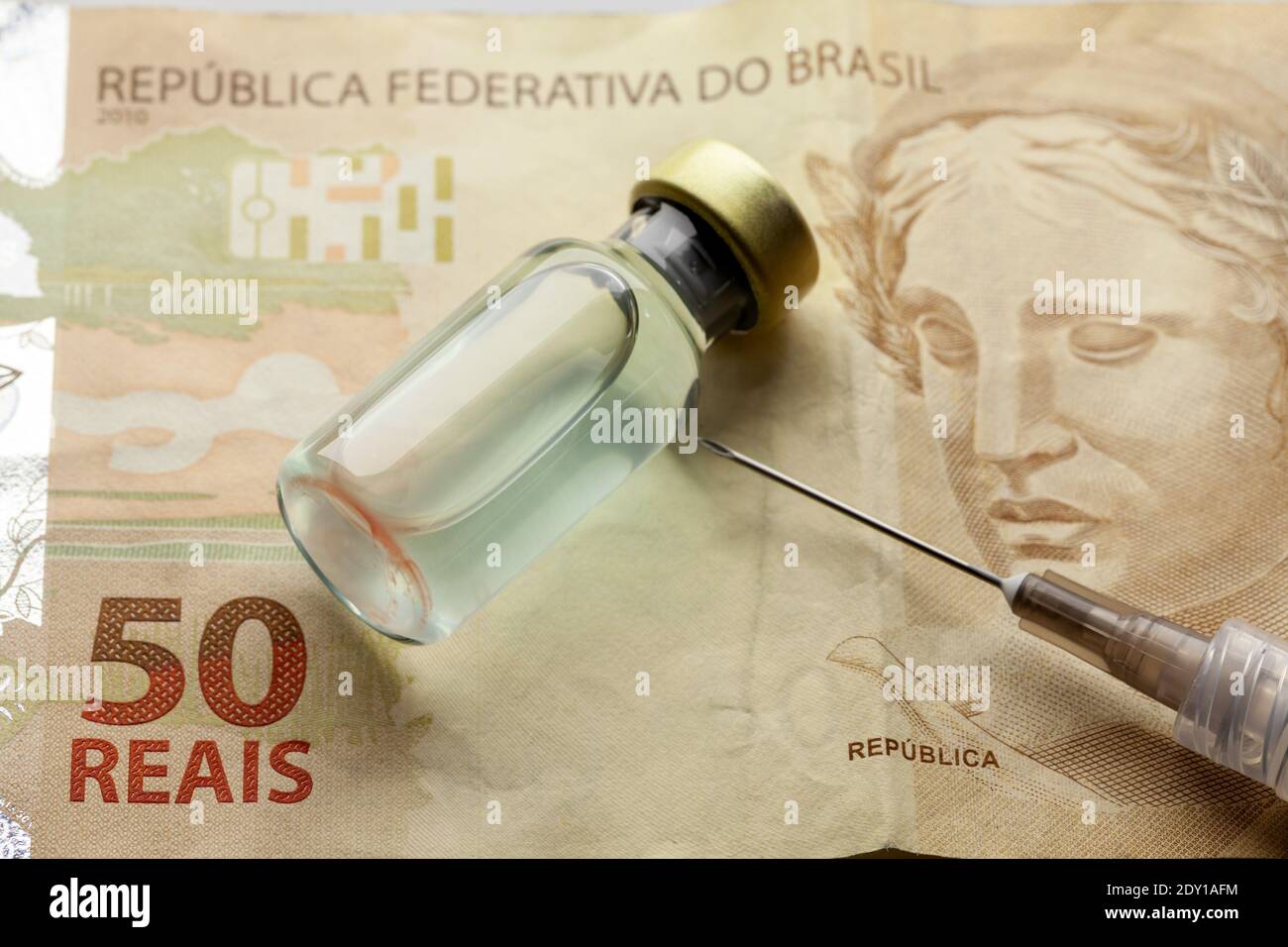 Glass vaccine bottle with liquid and syringe needle over a brazilian '50 Reais' bank note from close Stock Photo