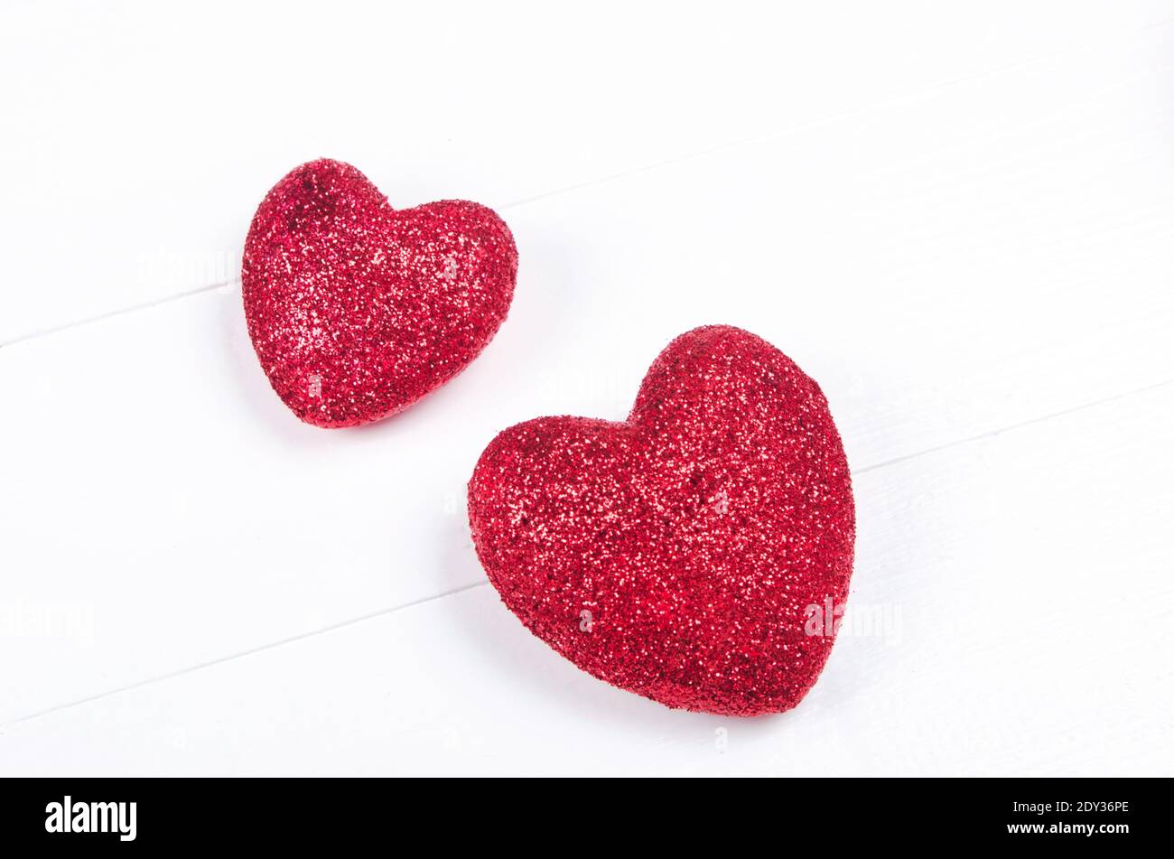 Two red glittering hearts on white wooden background. Stock Photo