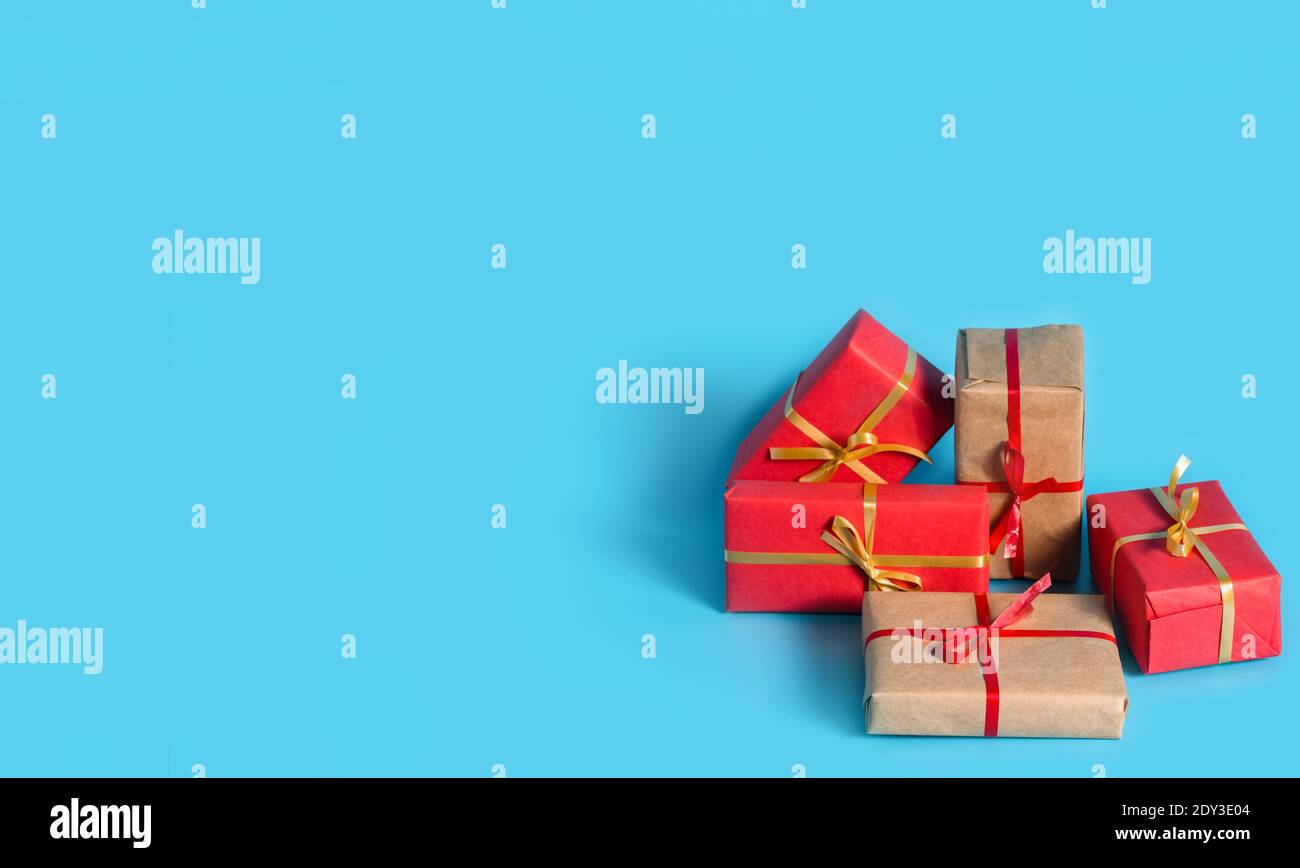 A lot of boxes with gifts in red and natural paper with gold and red ribbons on blue background. Copy space. Banner Stock Photo