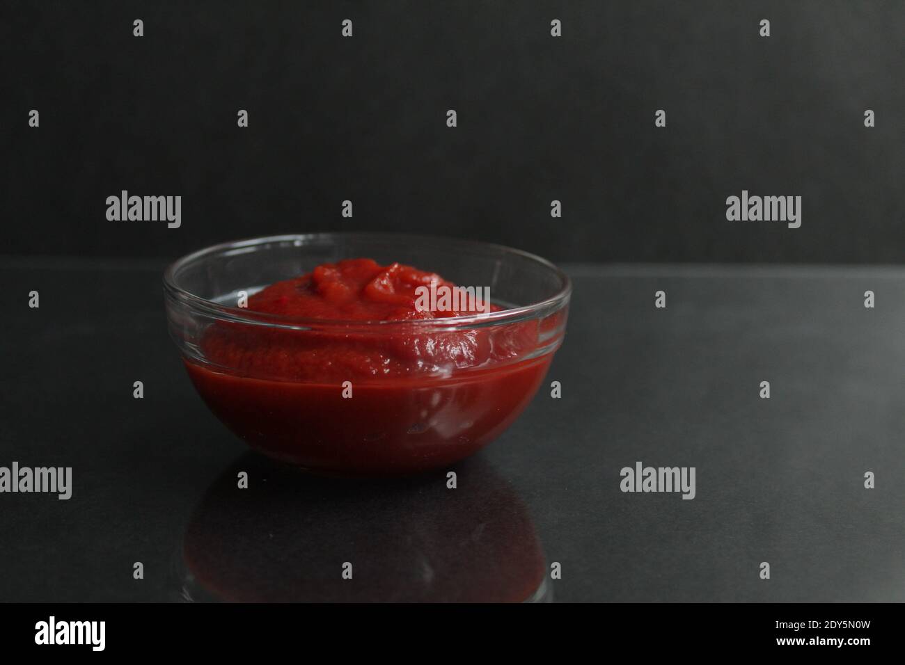 red tomato sauce paste in a glass sauce bowl on a black background copy space place for text. Stock Photo