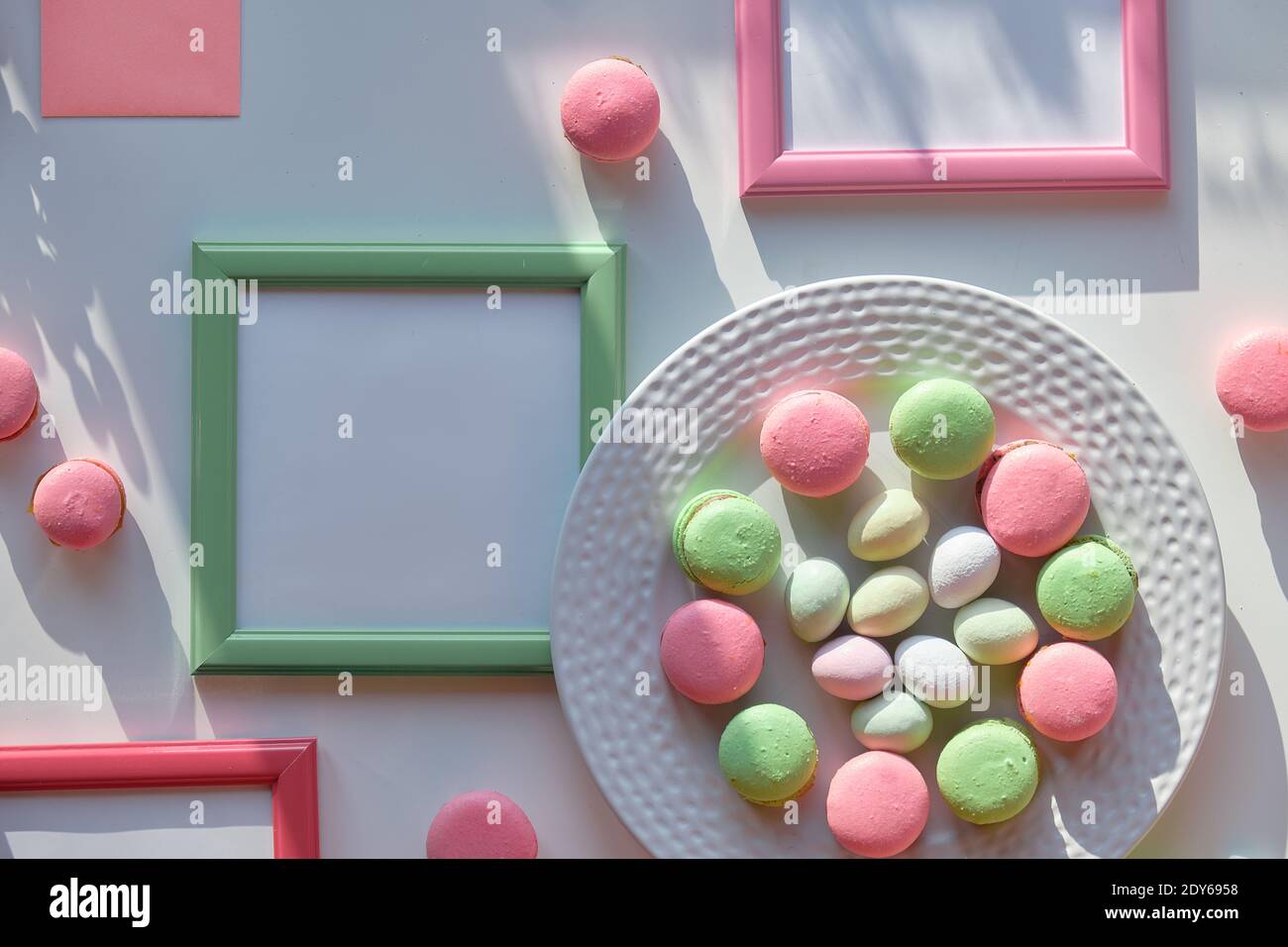 Easter sweets on white background with long shadows. Marzipan Easter eggs, pink and mint green macaroons on white plate. Text space in picture frames Stock Photo