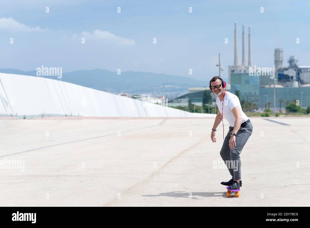 Bearded man with headphones enjoys riding a skateboard through city Stock Photo
