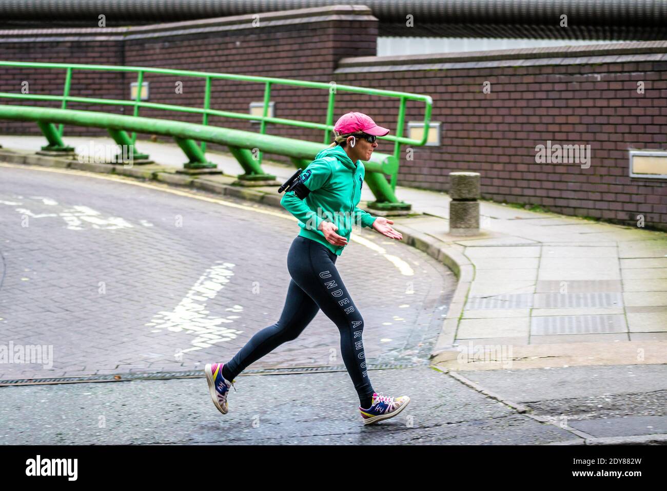 Woman jogging wearing Under Armour leggings, Kybun Cirrus DXB trainers /  sneakers, a green jacket, pink baseball cap and sunglasses Stock Photo -  Alamy