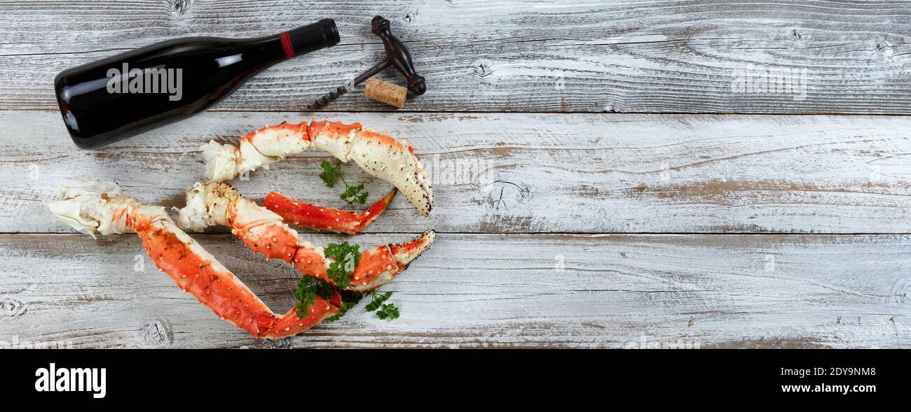 King crab claws and legs with wine bottle on white rustic wood in flat