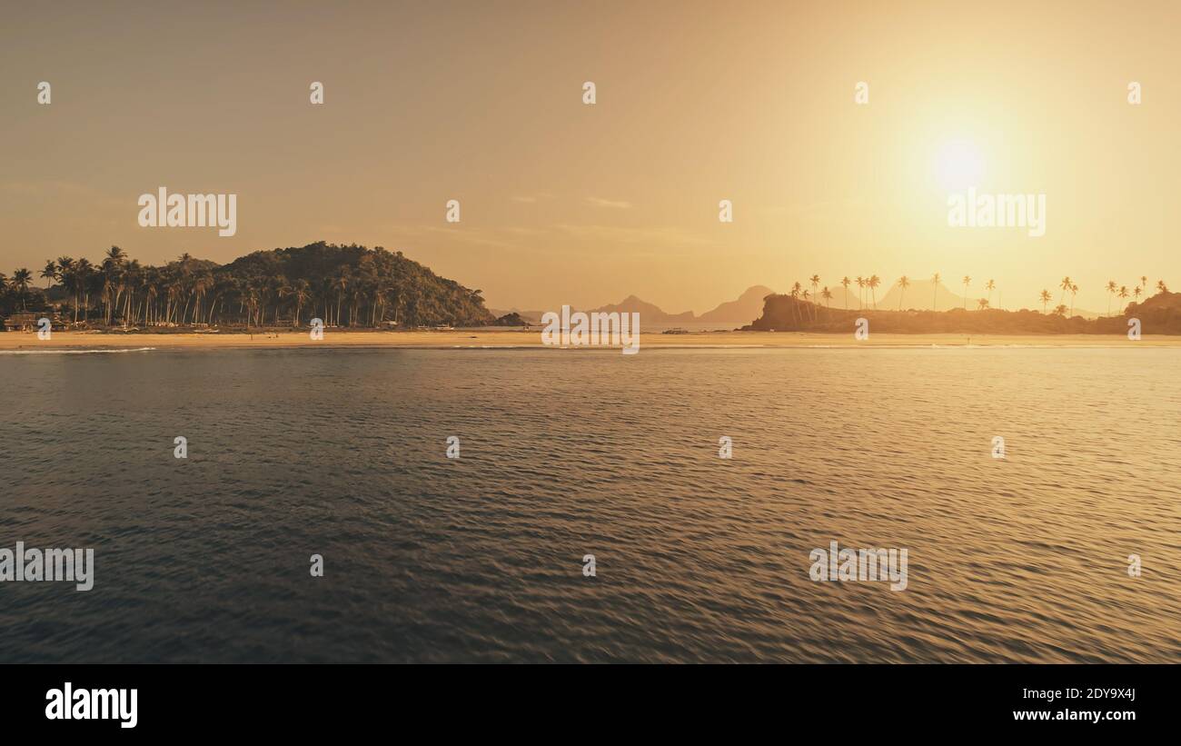 Sunset seascape at sand beach aerial. Summer tourist vacation at tropic paradise island with palm trees at sea shore. Nobody nature landscape of El Nido Islet, Philippines. Cinematic drone shot Stock Photo