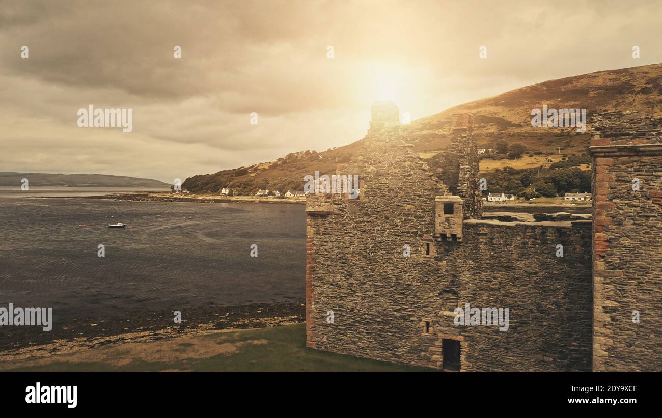 Closeup sun over castle ruins at sea bay aerial. Nobody nature seascape with boats. Historic heritage of United Kingdom. Cinematic Loch-Ranza, Arran island, Scotland, Europe. Cinematic drone shot Stock Photo