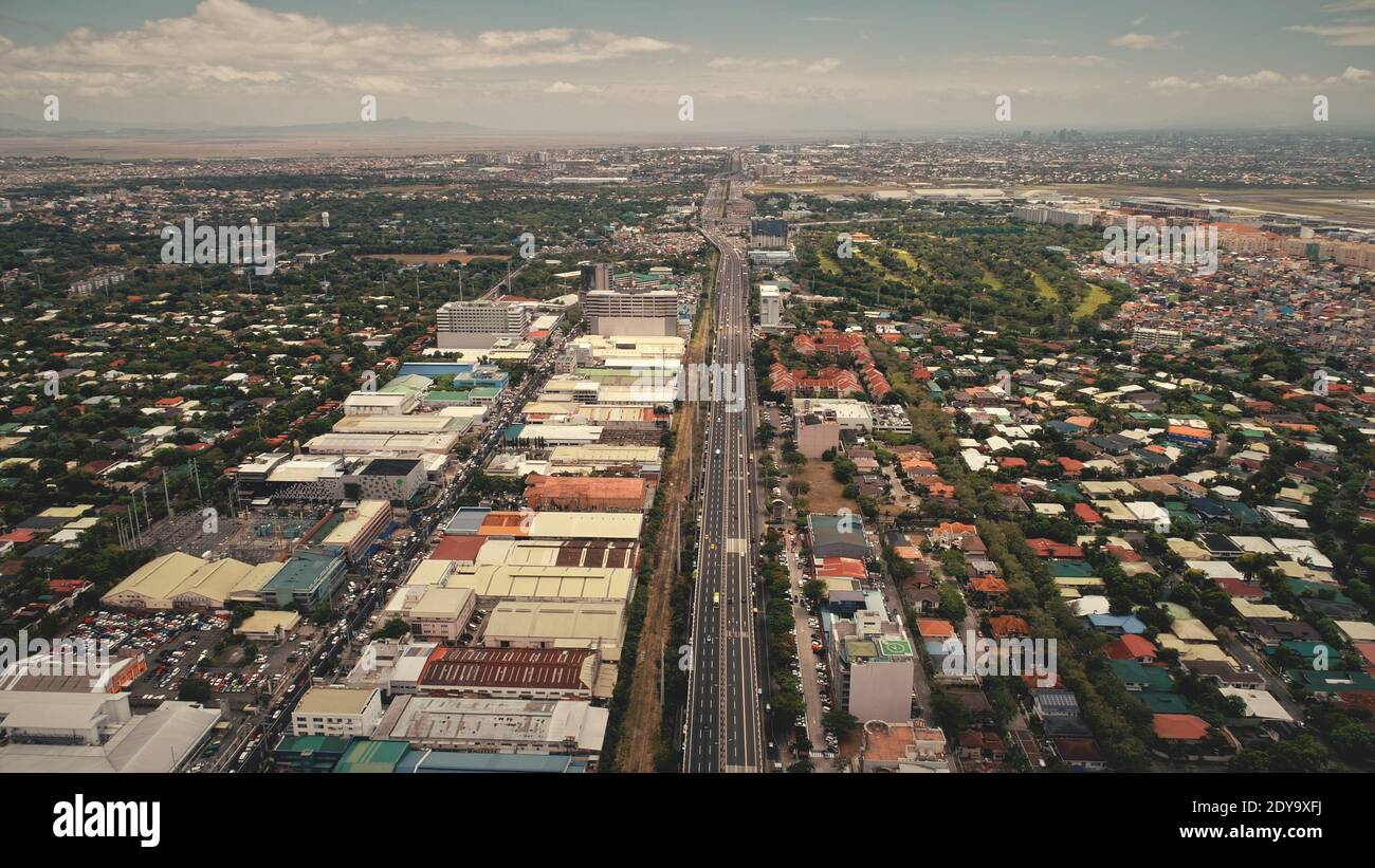Urban cityscape with streets at traffic roads and green trees at buildings in aerial view. Capital of Philippines and social, cultural, economic centre - Manila town scenery. Cinematic drone shot Stock Photo