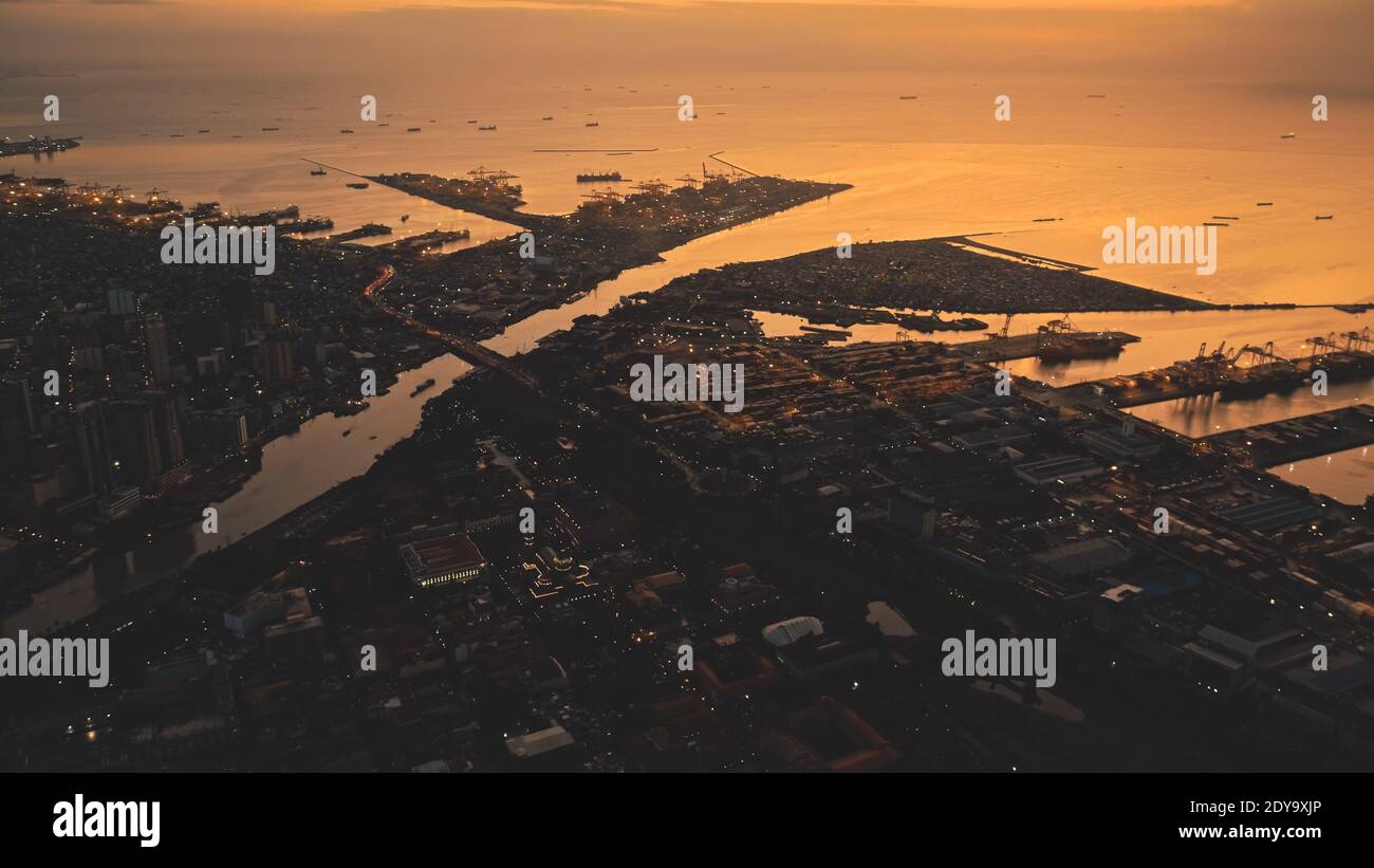 Sunset over sea bay at pier city aerial. Tropic cityscape on river banks at summer sun set light. Streets with buildings at traffic highway. Philippines metropolis town of Manils at drone shot Stock Photo
