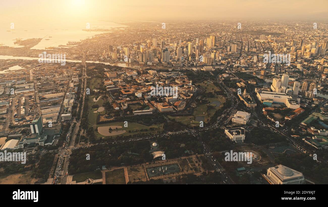 Sunset of port town at sea bay aerial. Pier city at river bank in sun set light. Metropolis cityscape of Manila city, Philippines, Asia. Modern buildings at design park of downtown streets Stock Photo