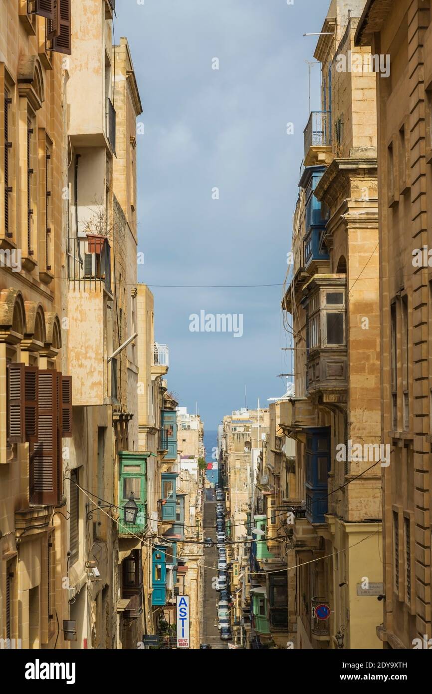 Long narrow street and old architectural apartment buildings with Maltese balconies, Valletta, Malta Stock Photo