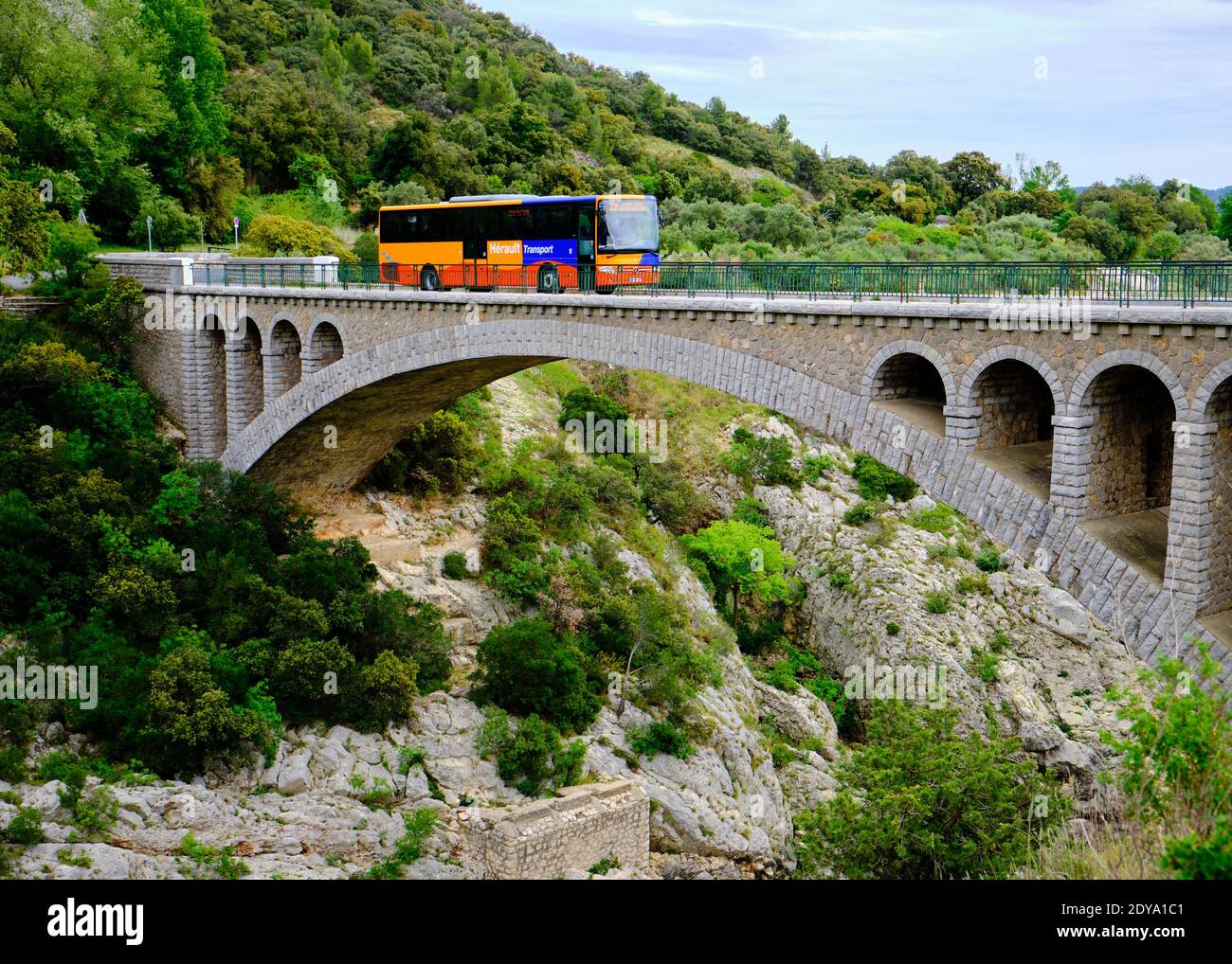 Herault Transport bus crossing the Pont du Diable (Devil's bridge) crossing rocky Herault Gorges near Saint Guilhem le Desert Stock Photo