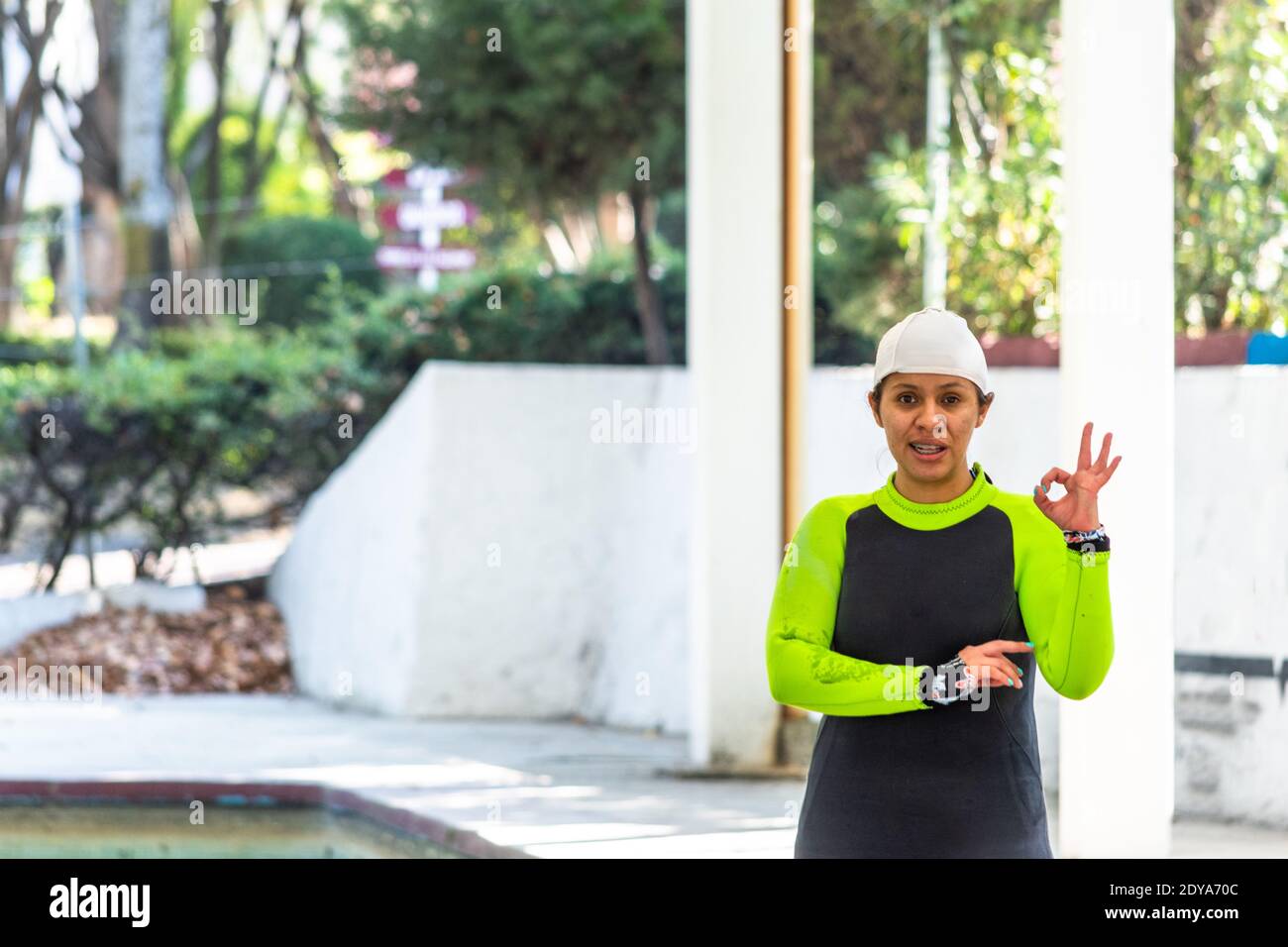woman after diving class standing in her black and green wetsuit by the pool making a hand sign Stock Photo