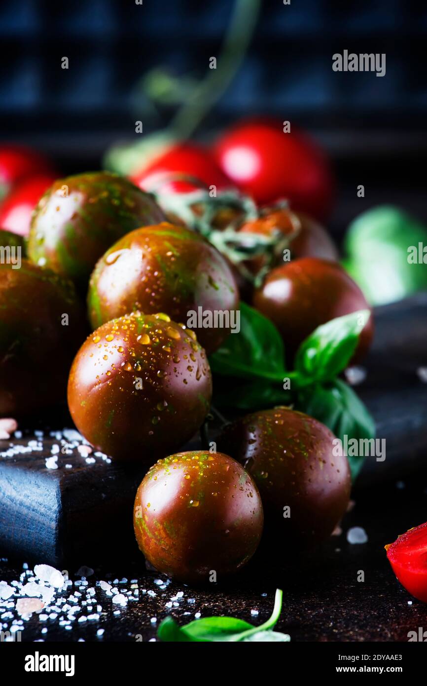 Brown cherry tomatoes with sea salt and green basil on dark table ...