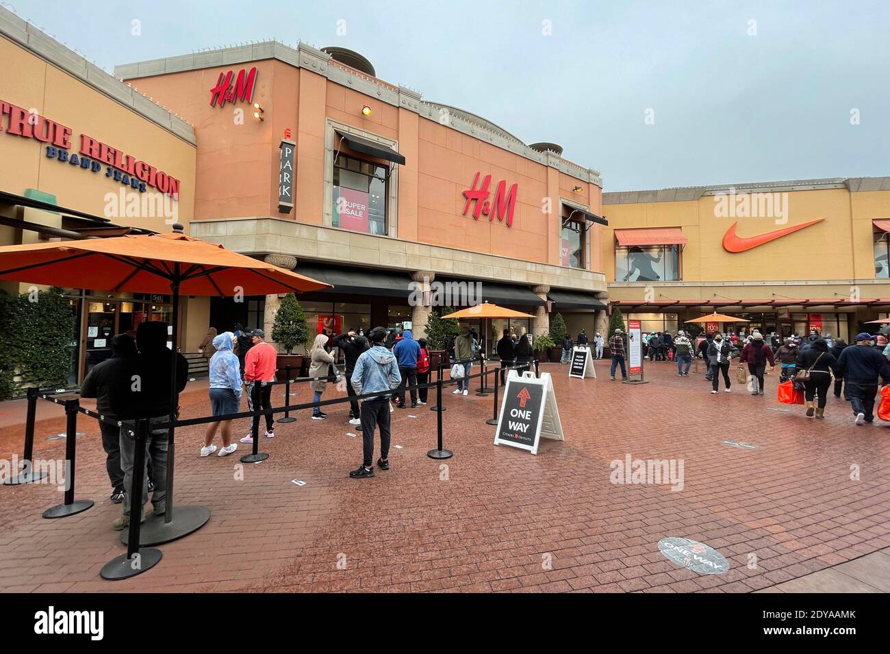 People stand in line outside the True Religion Brand Jeans, H&M and Nike stores the day before Christmas at the Citadel Outles amid the global coronav Stock Photo
