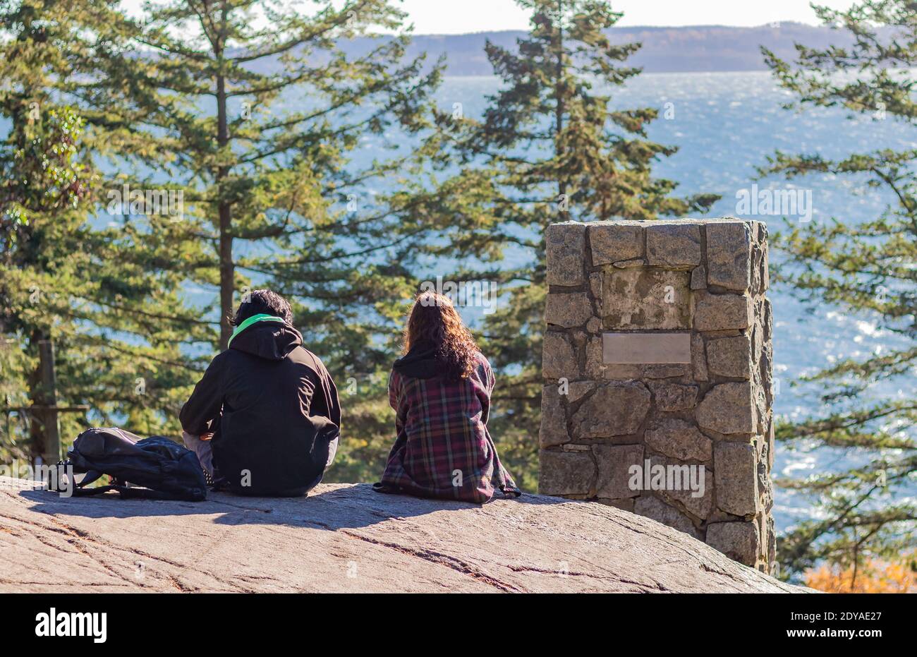 Back view of the young couple sitting on top of the hill with beautiful view of the sea. Stock Photo