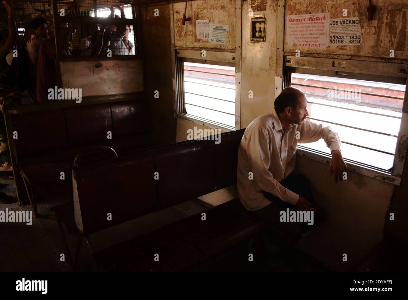 Chennai, Tamil Nadu, India - March, 2014: Man sitting on bench near window in suburban train. Crowd of people standing on exit door. Chennai city metr Stock Photo