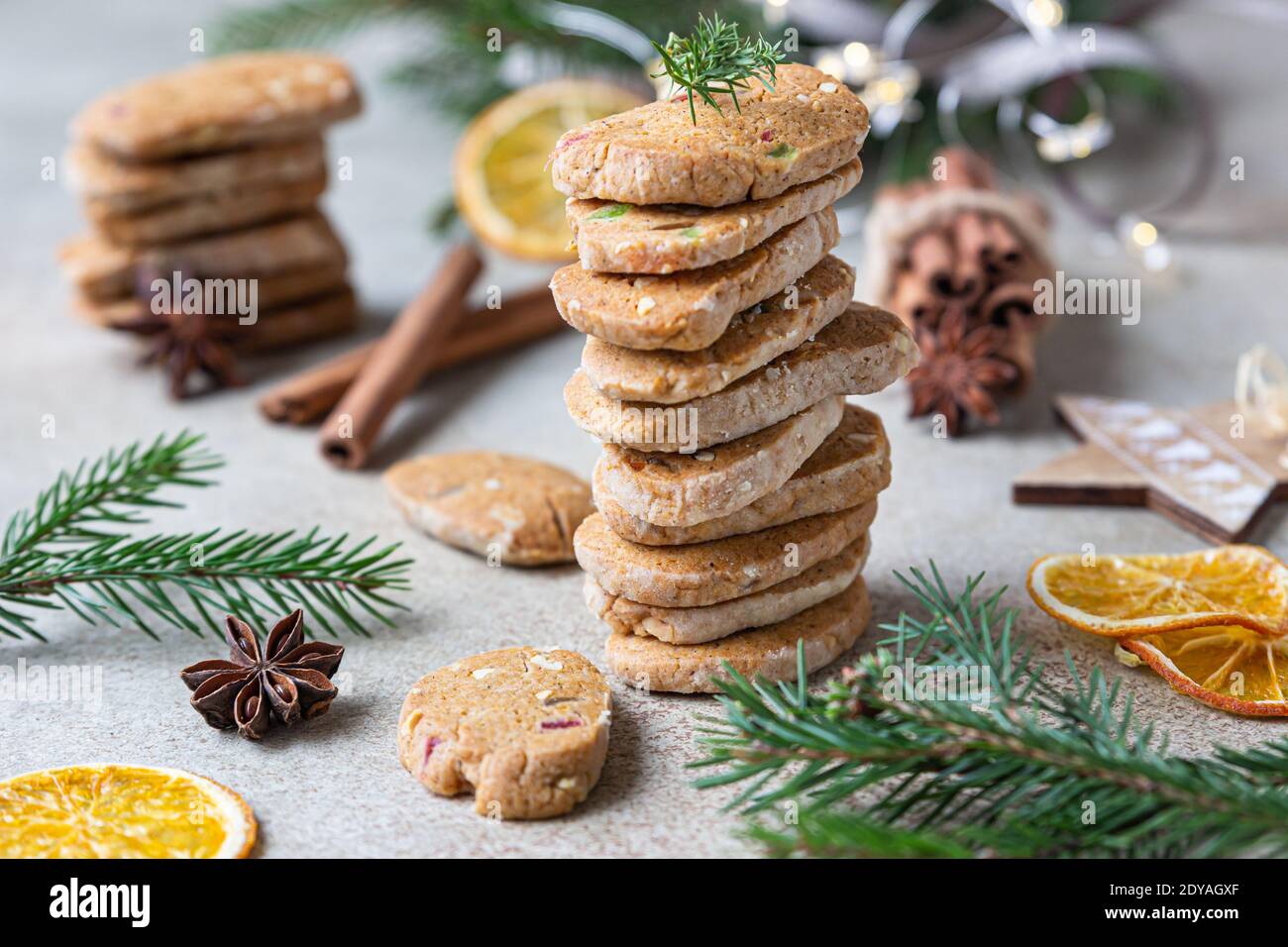 Stacked spicy butter cookies with candied fruits, cinnamon sticks and anise. Festive Christmas or New Year background with fir branches and dried oran Stock Photo