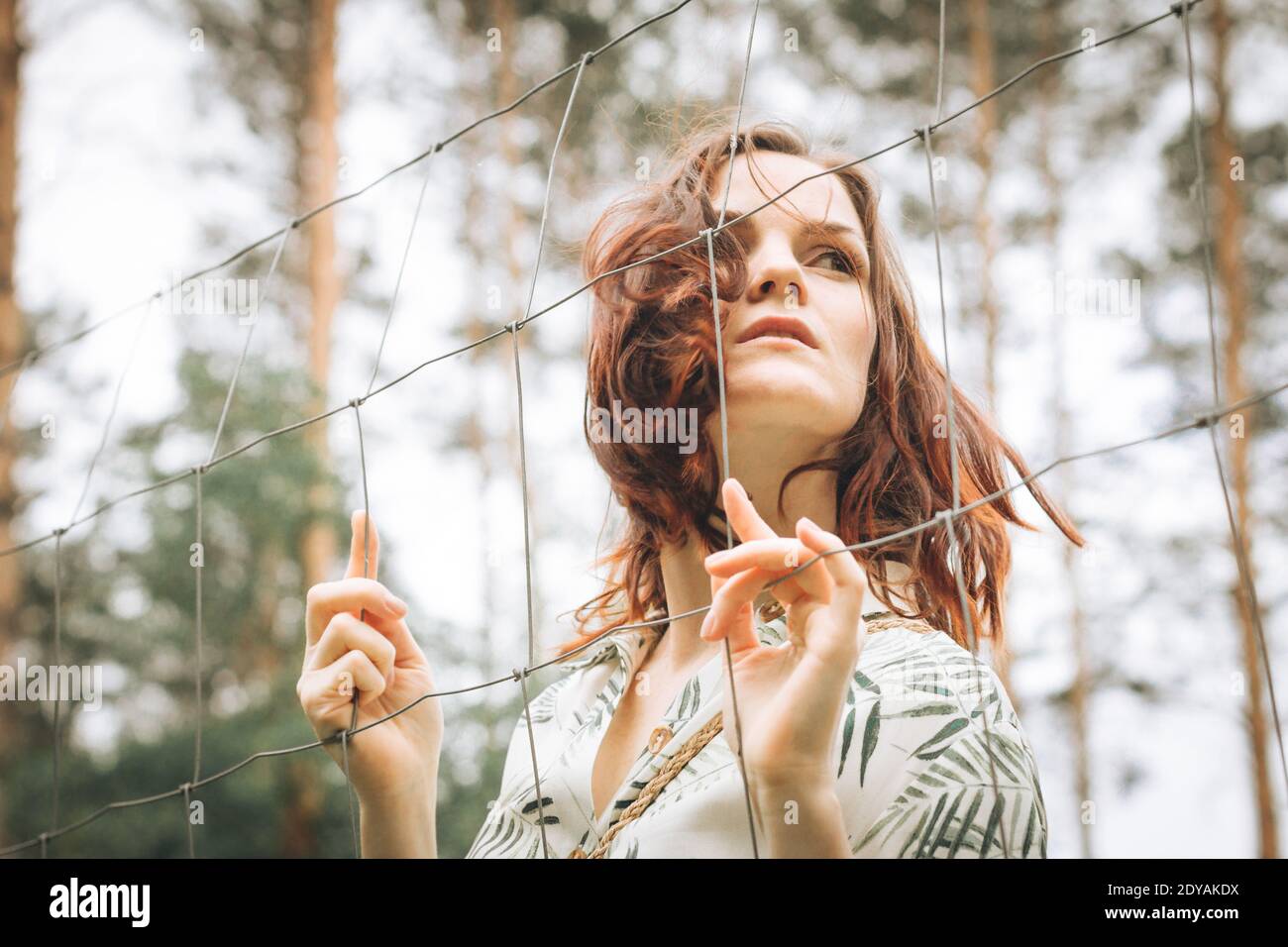 Redhead girl behind a fence outdoors. Psychology, phobias or fears Stock Photo
