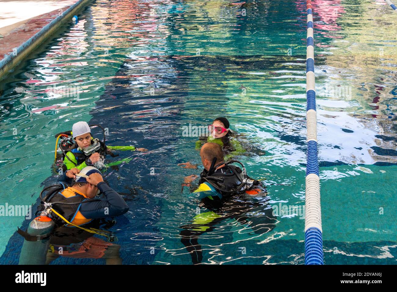 a group of four divers with all their equipment on talking inside the pool Stock Photo