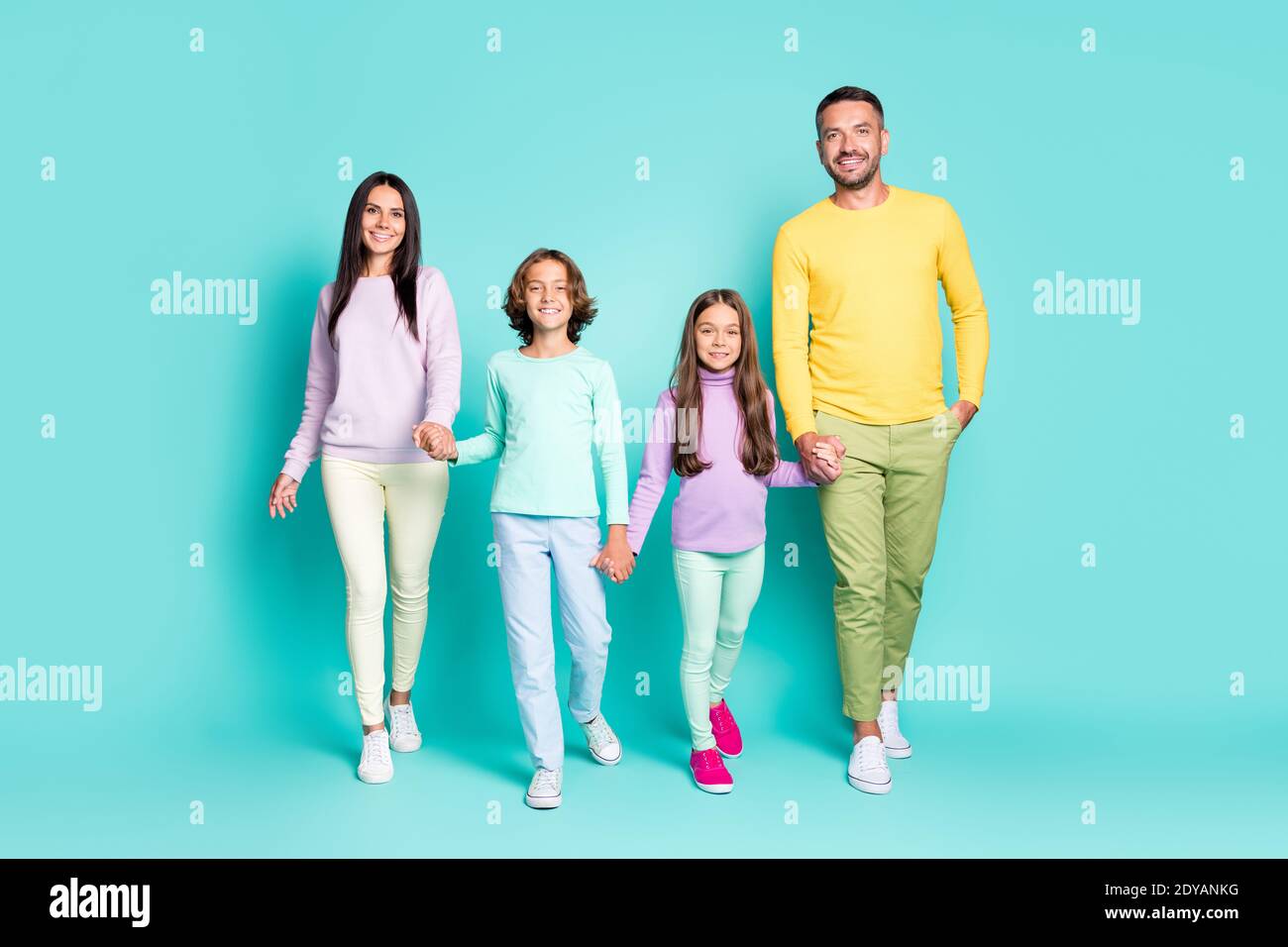 Photo portrait of full family walking forward holding hands isolated on vivid teal colored background Stock Photo