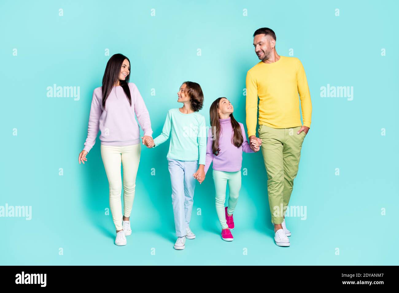 Photo portrait of full family looking at each other holding hands walking isolated on vivid cyan colored background Stock Photo