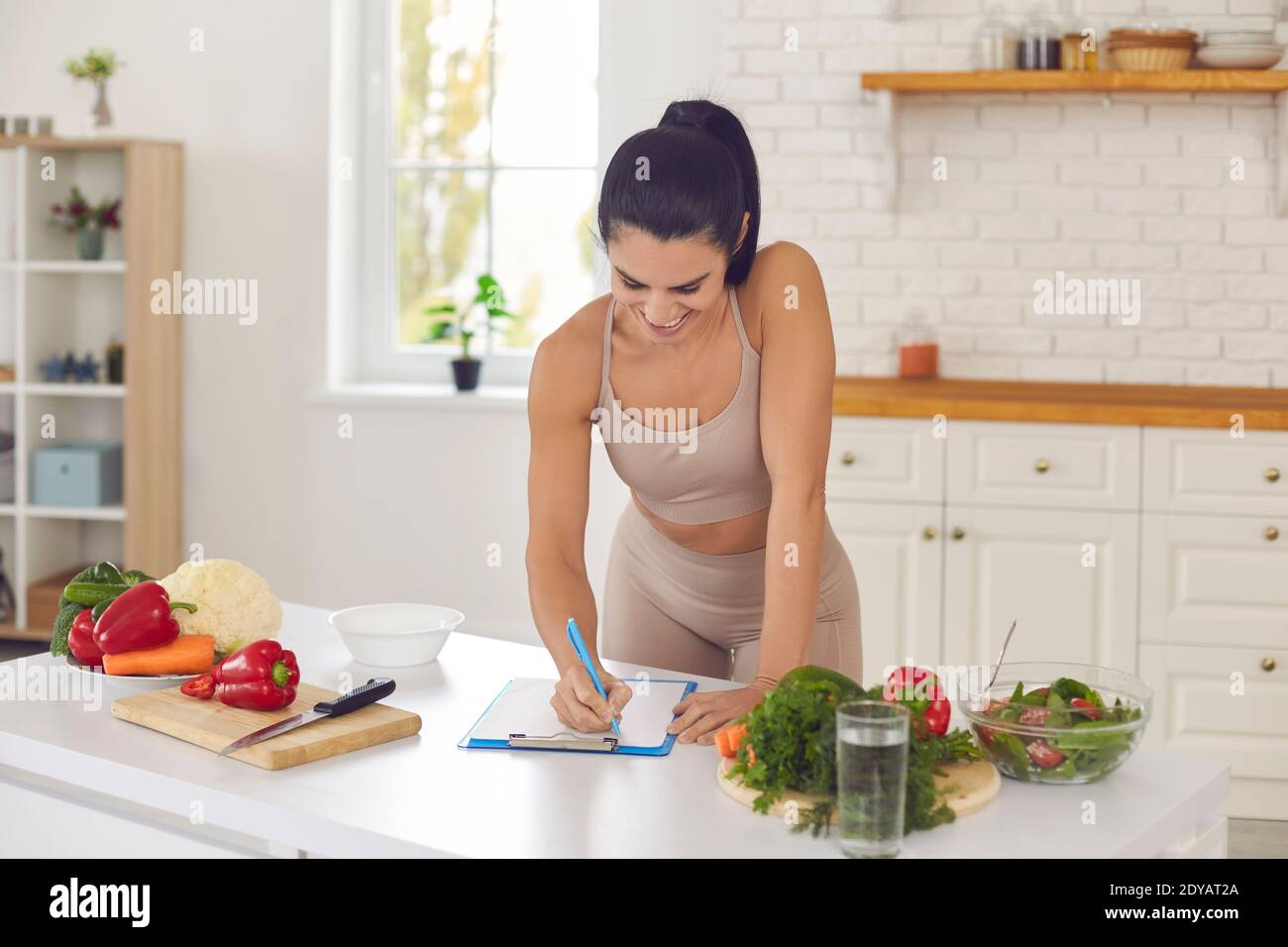 Cheerful pretty slim female athete writing down healthy recipe at home Stock Photo
