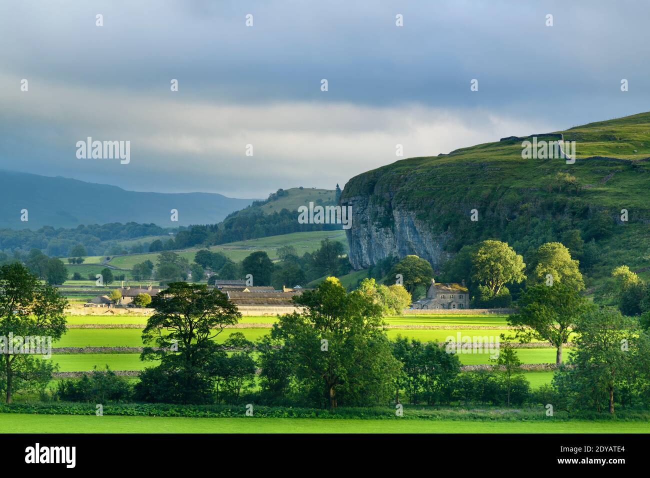 Scenic Wharfe Valley (flat sunlit fields, stone walls, Kilnsey Crag - high limestone cliff, rolling hills) - Wharfedale, Yorkshire Dales, England, UK. Stock Photo