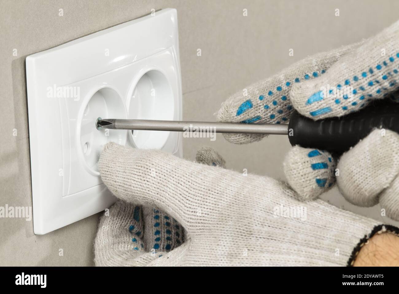 electrician's hands with a screwdriver fix the electrical outlet on drywall, closeup Stock Photo