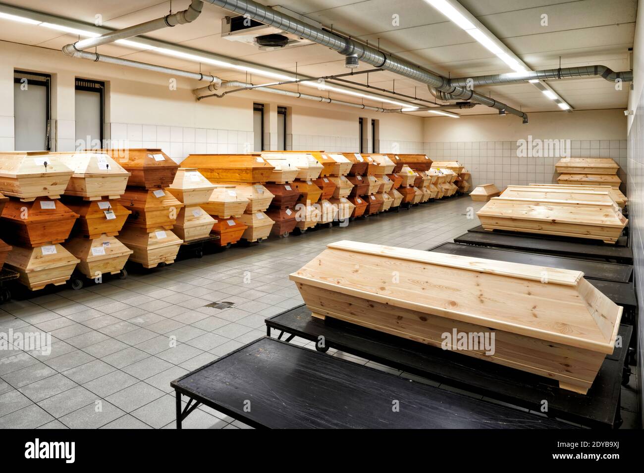 In einem kuehlen Raum eines Krematoriums stapeln sich Saerge mit Toten die noch eingeaeschert werden sollen. Die Sargreihen verlaufen an den Waenden e Stock Photo