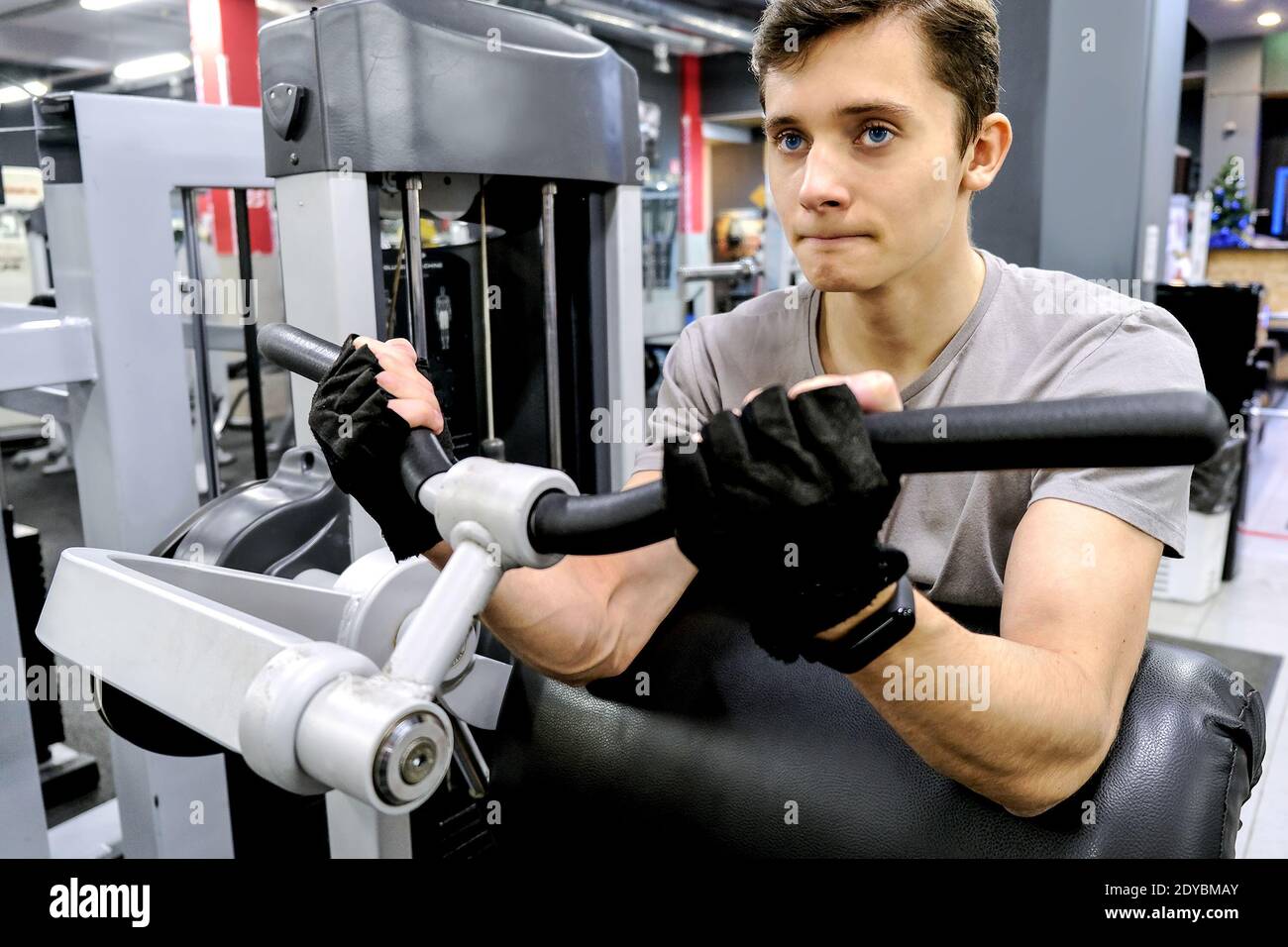 A young man exercises on the simulator in the gym. Trains the muscle strength. The concept of a healthy lifestyle Stock Photo