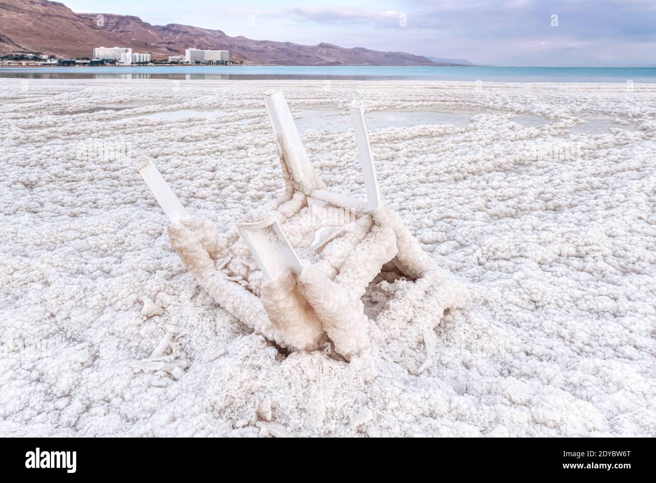 Small plastic chair completely covered with crystalline salt on shore of dead sea, closeup detail, blurred hotel resorts in distance - Ein Bokek Stock Photo