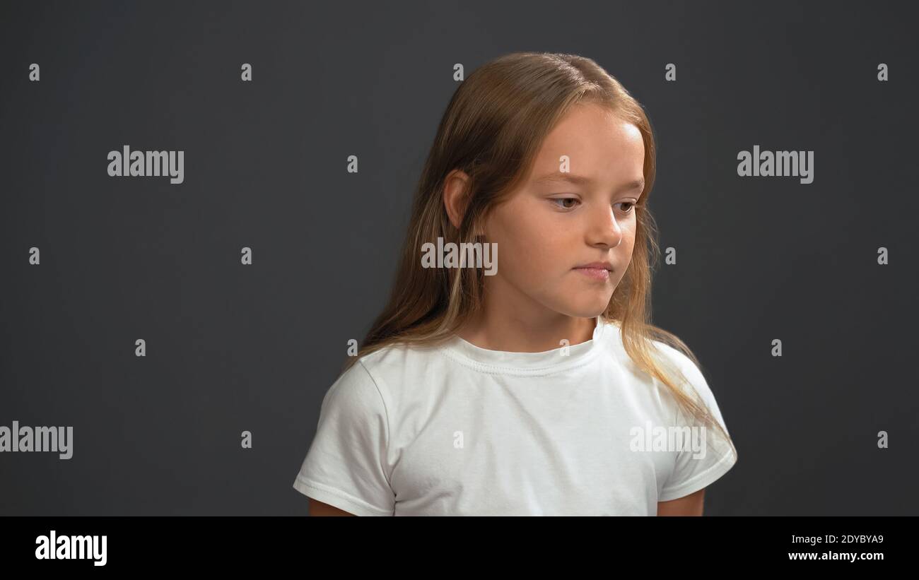 Disappointment little girl with long blond hair, looking thoughtful down wearing white t-shirt and black pants isolated on black background Stock Photo