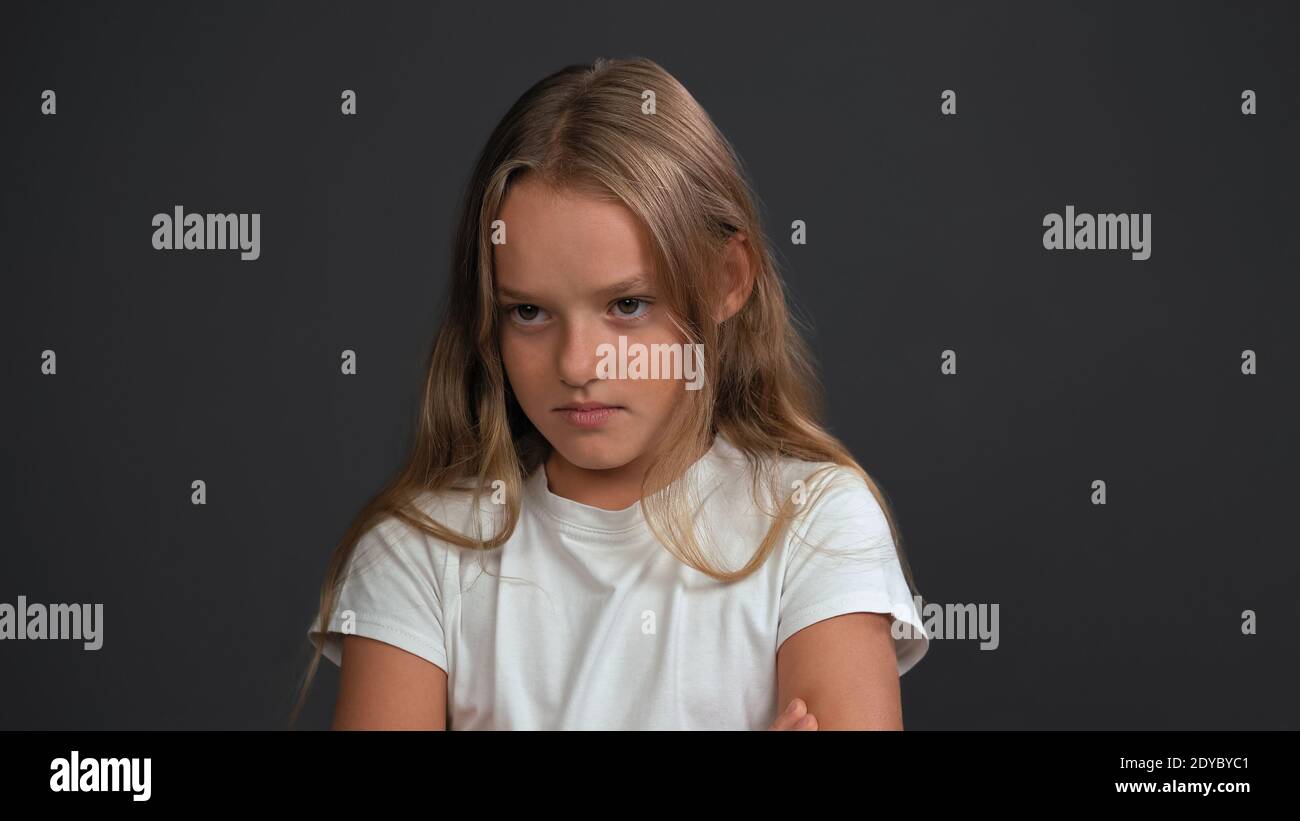 Disappointment on the face of a lovely baby little girl with hands folded, looking at the camera wearing white t-shirt and black pants isolated on Stock Photo