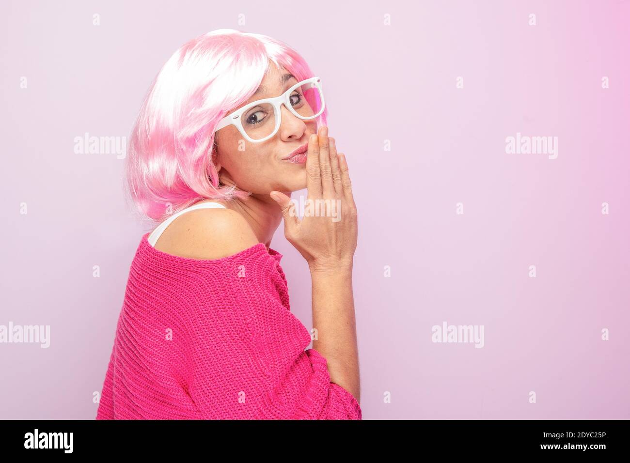 Caucasian woman with pink wig and sweater, wearing white glasses, posing funny at the photo studio. Funny expressive women and colorful portrait conce Stock Photo