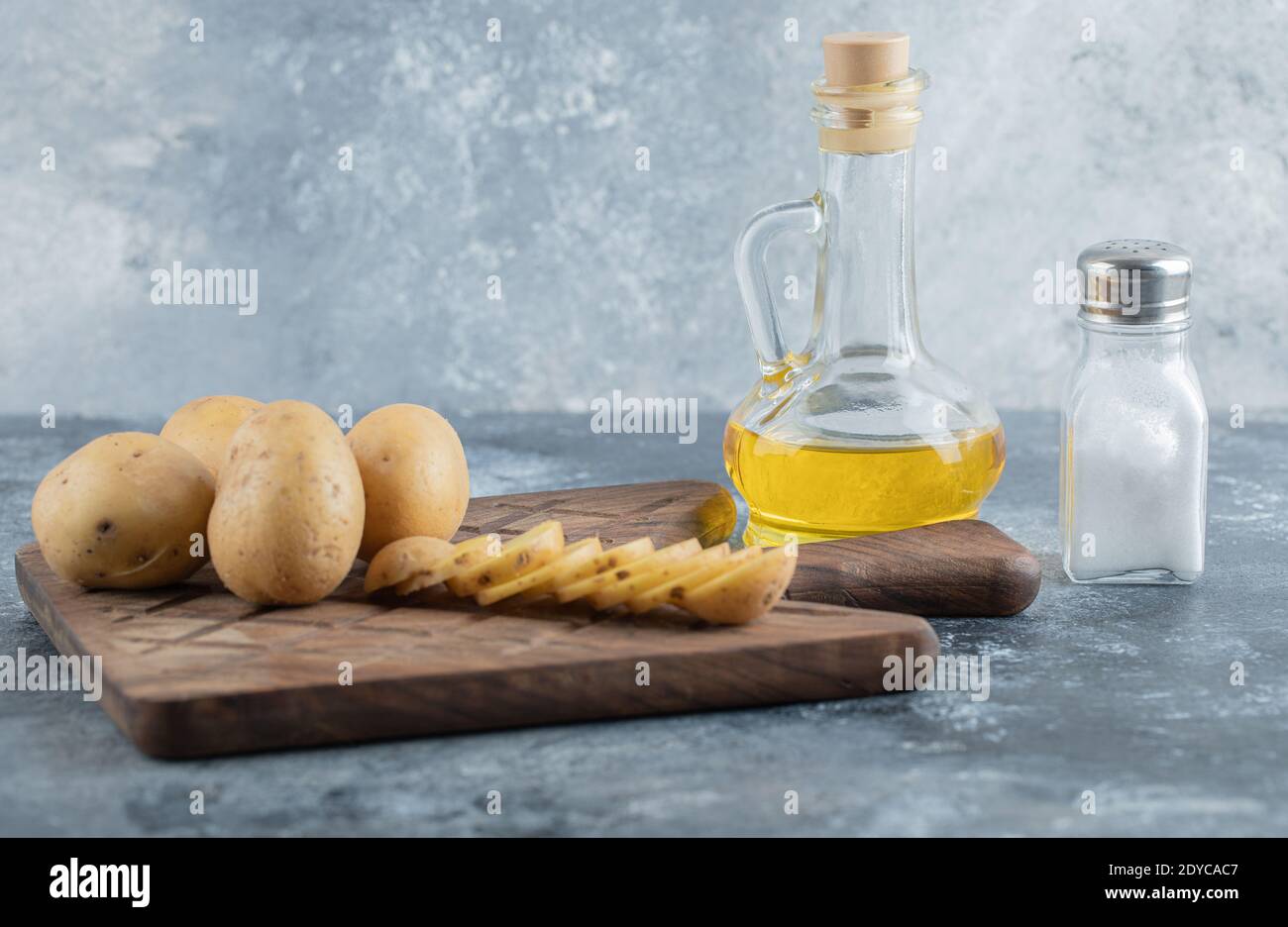 Sliced and whole potatoes on the cutting board with oil and salt Stock Photo