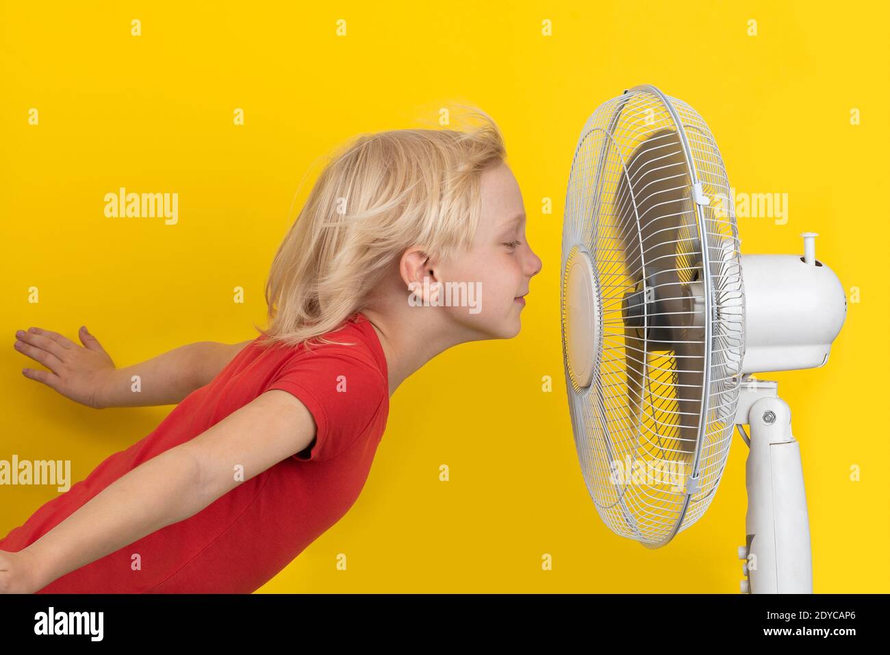 Boy enjoying cool air. Child and fan on yellow background. Room