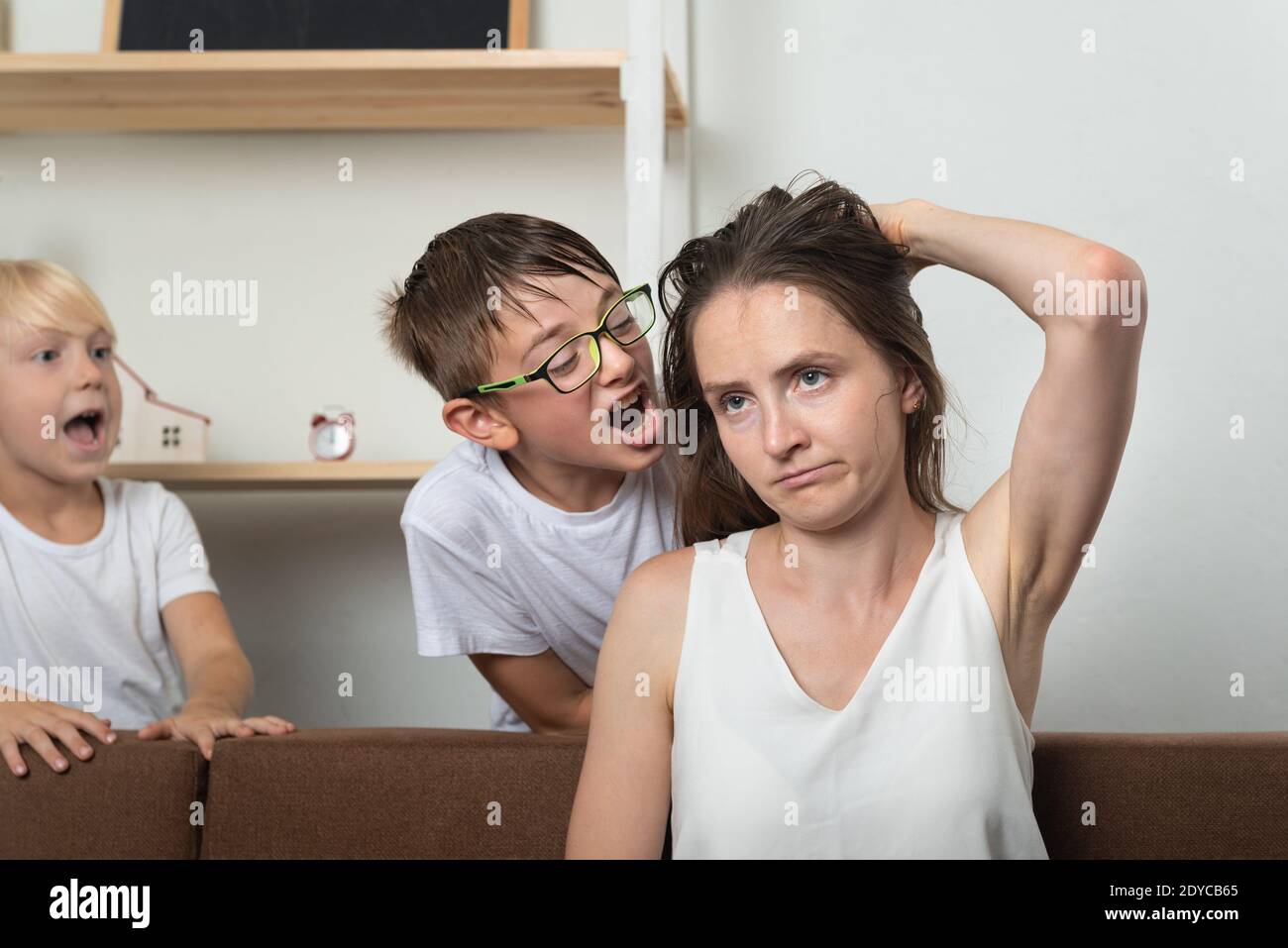 Tired mother sitting on couch feels annoyed exhausted while children