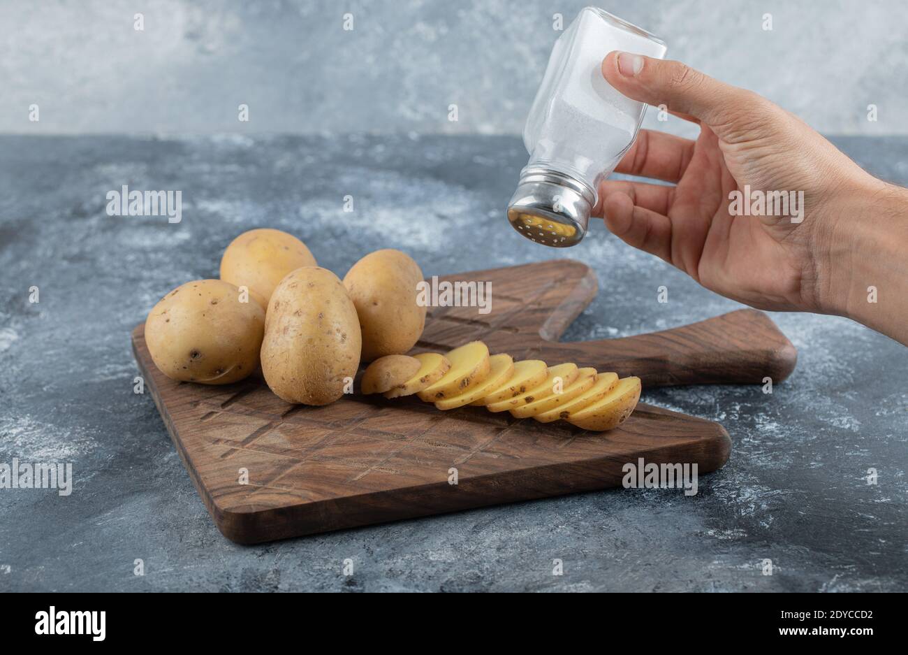 Man pouring salt over the sliced potatoes Stock Photo