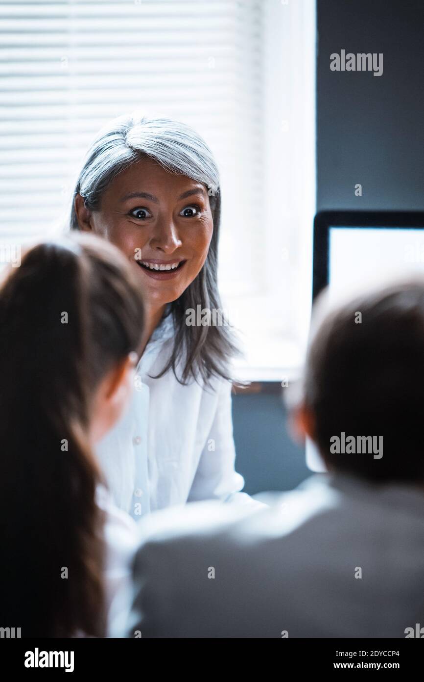 Mature Asian supervisor woman cheerfully talking to employees sitting one against another. Asian mature business woman talking to a managers sitting Stock Photo