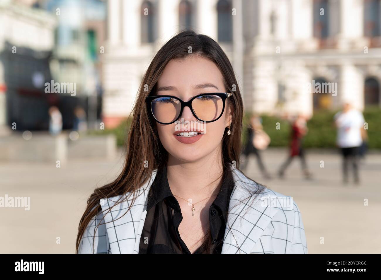 Portrait of young brunette woman wearing glasses. Student against institute background. Postgraduate teacher. Stock Photo
