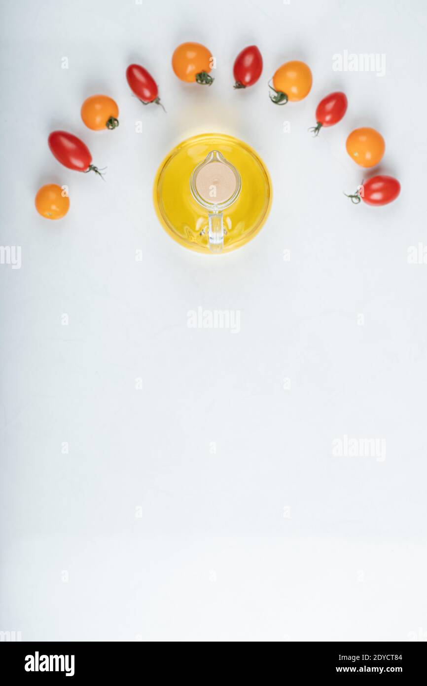 Gleaming red and yellow tomatoes on white background with bottle of oil ...