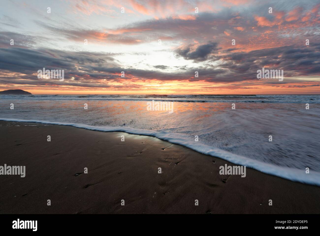 Golden sunrise across the ocean on Wainui Beach New Zealand Stock Photo