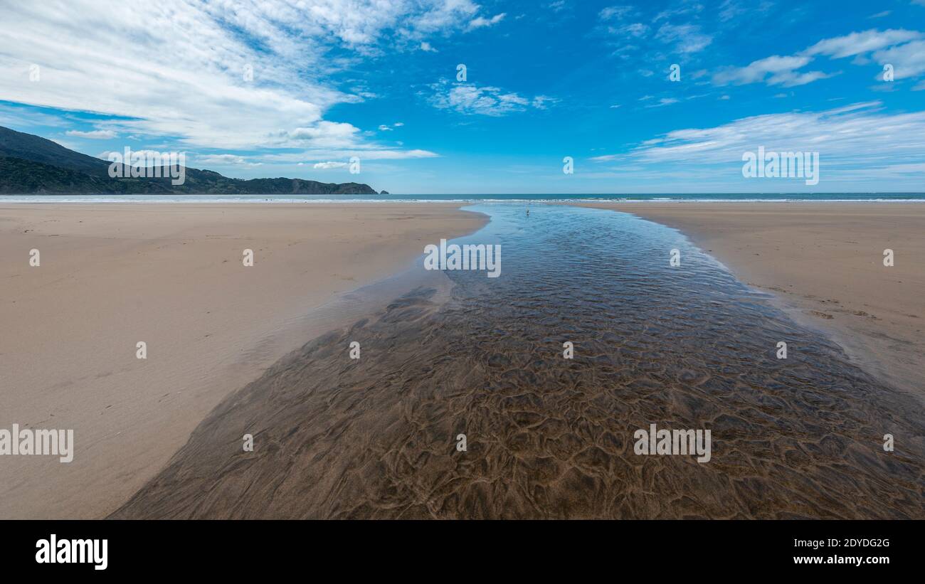 Water flowing down a sandy beach into the sea under a blue sky Stock Photo