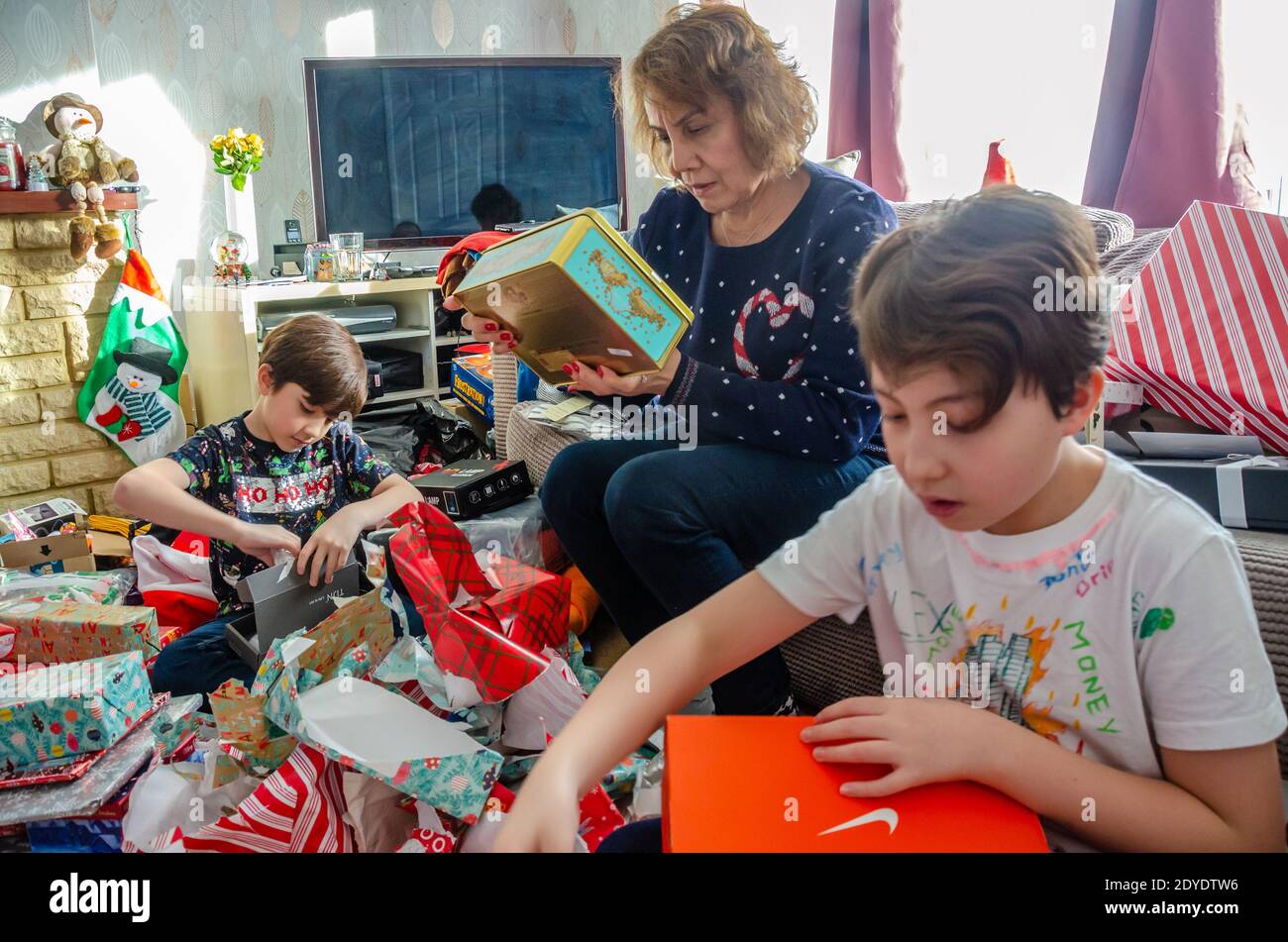A family excitedly open Christmas presents together at home on Christmas day. Stock Photo