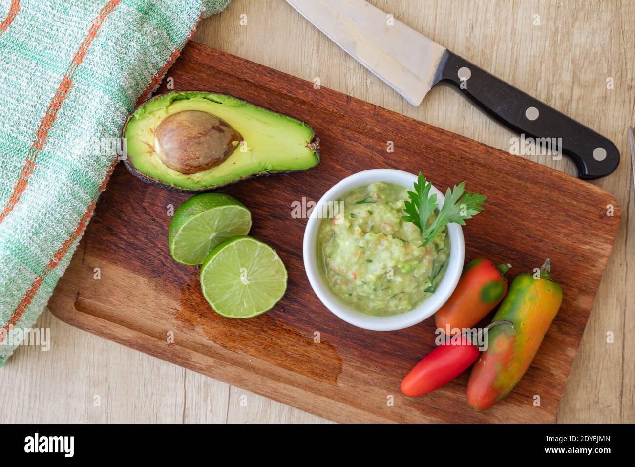Half avocado, some hot peppers and a lime on a wooden board and bowl with the guacamole sauce Stock Photo